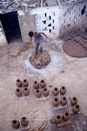 Image du Maroc Professionnelle de  Un ouvrier pétrit l’argile imprégnée d’eau à côté d'objet en poterie qui sèchent au soleil avant une première cuisson dans les fours des ateliers de la Colline des Potiers à Safi, Vendredi 29 Août 1997. (Photo / Abdeljalil Bounhar)